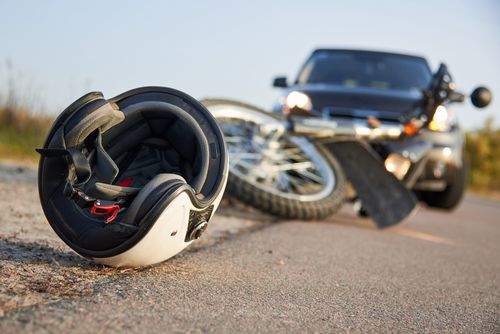 Motorcycle helmet on road next to crashed motorcycle and car concept of Fairburn motorcycle accident lawyer